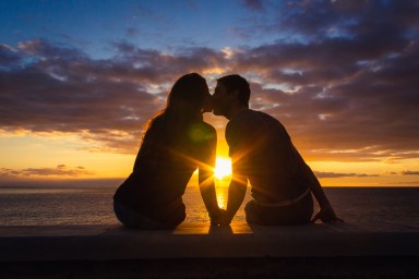 Man and woman sitting by the sea kissing at sunset at Meloneras beach walk, Gran Canaria