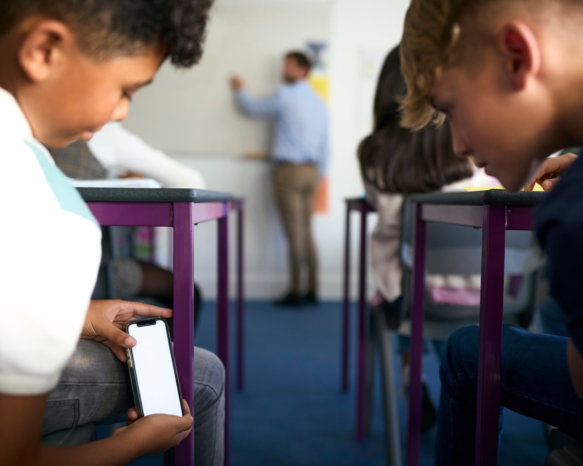 Close Up Of Two Male Secondary Or High School Pupils Looking At Mobile Phone During Lesson